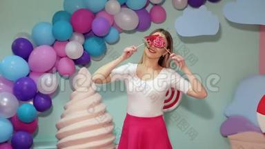 一个穿着亮衣服带棒棒糖的女孩，她用大棒棒糖遮住眼睛。