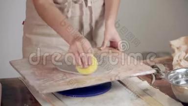 雕塑家的女人正在给粘土浇水，并为未来的盘子和特写塑造边缘