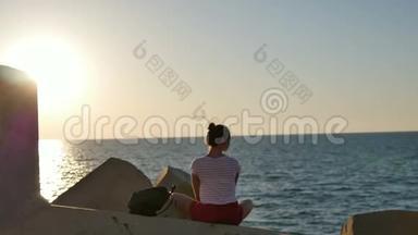 梦中的年轻女子坐在岩石上享受日落时的大海