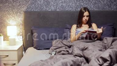 美丽的年轻女孩躺在卧室的床上，读一本烹饪书。 晚上在家休息的女人。