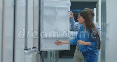 一男一女打开冰箱门检查设计和质量，然后再在商店购买
