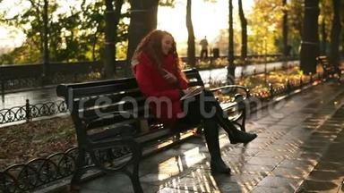 年轻的女士<strong>正在看书</strong>，红头可爱的女孩正坐在公园的长椅上，秋天五彩缤纷的景色，镜头耀斑，放松一下
