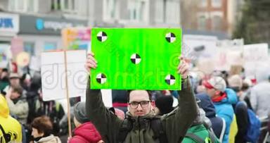 在城市示范中，年轻人在人群背景上拿着绿色屏幕的海报。