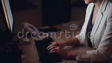 一张严肃的年轻女人在电脑打字，看着屏幕，独自坐在黑暗的工作台上的倾斜镜头