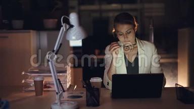 穿着正式服装的漂亮<strong>女</strong>孩独自在笔记本电脑上工作，在黑暗的办公室<strong>深夜</strong>完成紧急工作
