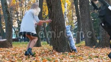年轻的妈妈穿着裙子和她的小宝宝在秋天公园玩捉迷藏。