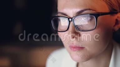 在黑暗的办公室里，一位戴着眼镜、深夜用电脑工作的年轻美女特写镜头