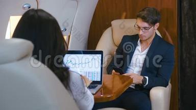 成功的商人驾驶私人飞机。 在笔记本电脑上工作。 使用智能手机。 商人和女商人
