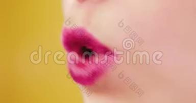 特写粉嫩透亮的女唇.. 那个女人在工作室里的黄色背景上亲吻和微笑。 爱，空气