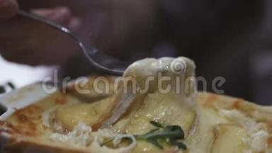 在叉子上特写热拉伸奶酪。 一个年轻的女人坐在餐馆里吃热千层面。