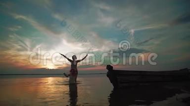 慢动作。 日落时分，一个女人和一个小孩在湖面上欢快地奔跑。 小孩子的剪影