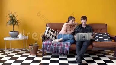 漂亮的年轻夫妇坐在沙发上的笔记本电脑上。 库存录像。 几个<strong>学生一起</strong>看