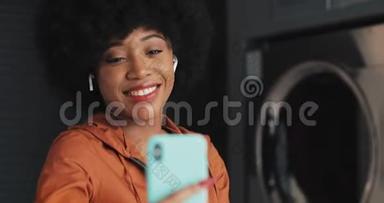 快乐迷人的非裔美国年轻女子在自助洗衣店视频聊天。 自助公共洗衣店。