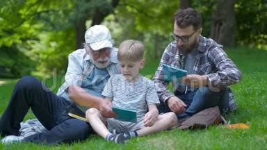 <strong>三代</strong>幸福的家庭——父亲、祖父和金发儿子坐在公园的草地上，带着书学读书