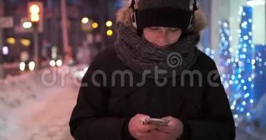 <strong>冬天寒冷的</strong>夜晚，男人在户外使用手机和耳机