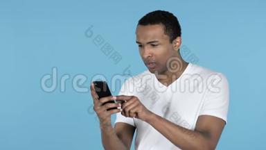 年轻的非洲男子应对损失和使用智能手机，蓝色背景