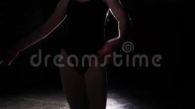 年轻的芭蕾舞演员站在聚光灯下，在工作室的黑色背景。 芭蕾舞表演经典的芭蕾舞表演。 慢动作