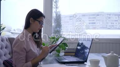 戴眼镜的女商人用手提电脑，在桌旁的<strong>笔记</strong>本上用蓝色记号笔写<strong>笔记</strong>