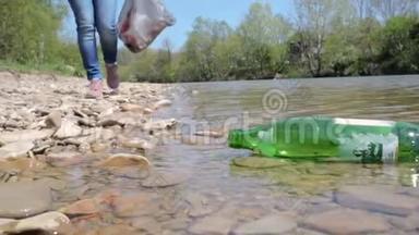 一个年轻的女人在河边收集垃圾，拿出一瓶水。 <strong>环境改善</strong>和