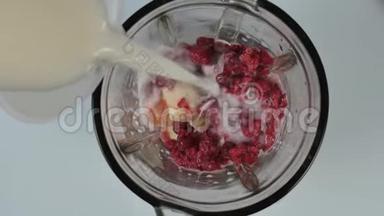 年轻女子在搅拌机里煮水果和浆果鸡尾酒。 用覆盆子在搅拌机里倒牛奶。 健康饮食