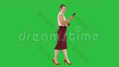 美丽的年轻女子正在使用智能手机上的一个应用程序发送短信，并在绿色屏幕上行走