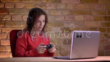 年轻的女博客写手穿着红色连帽衫，用操纵杆玩电子游戏，在布里克肯身上丢脸