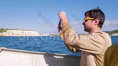 一位穿着米色毛衣的游客在海上的快艇上游泳，并在电话上拍照。 年轻人，旅游，旅游