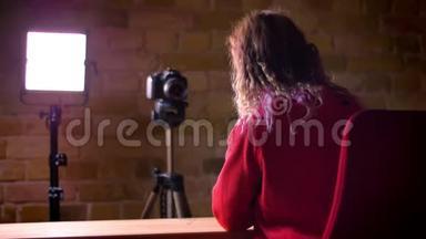 后景年轻博主在红色帽衫录制视频前相机和灯在布里克肯墙背景。