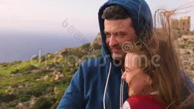 一位父亲在岩石和大海的背景下与女儿交谈，微笑，解释，拥抱。 家庭<strong>开支</strong>
