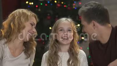 快乐的父母亲吻他们可爱的女儿的脸颊<strong>坐在</strong>圣诞<strong>树下</strong>