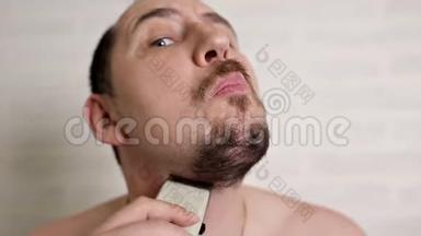 一个人用电动剃须刀刮大胡子。 一个人的特写肖像