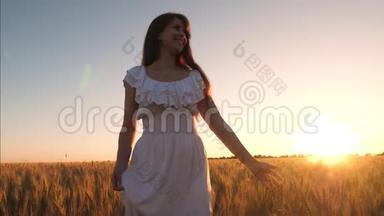穿着白色衣服的漂亮<strong>女孩</strong>正带着小麦在<strong>田野</strong>里散步，在夕阳的照耀下。 <strong>女孩</strong>的手触及成熟小麦的耳朵