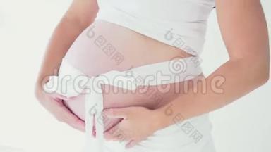 穿着内衣的怀孕妈妈在玩婴儿鞋。 带带的肚皮
