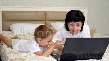 <strong>妈妈和宝宝</strong>躺在床上正在浏览笔记本电脑上的婴儿装备。 育儿、互联网<strong>和</strong>