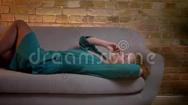 <strong>姜黄色</strong>卷发的白种人女孩躺在沙发上，在舒适的家庭背景下，在智能手机上愉快地交谈。