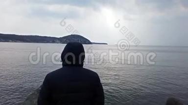 一个穿着蓝色夹克，带着兜帽看海景的人。 <strong>海参</strong>崴，普里莫斯基。