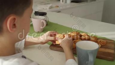 男孩在现代厨房吃早餐。 男孩吃带牛奶的饼干。 厨房里的白色桌子。 灰色碗在桌子上。 关门