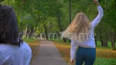 两个滑稽的白种人女孩在一起，在美丽的绿色公园里跳跃，扔出，跳舞和