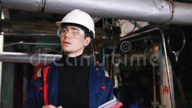 一个戴着头盔和<strong>防</strong>护<strong>眼镜</strong>的男工程师在制造厂做笔记