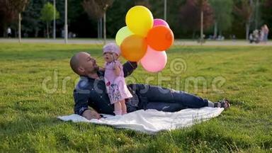 爸爸戴着气球的眼镜，小女儿躺在公园的毯子上，然后女儿摘下爸爸的眼镜，吻他