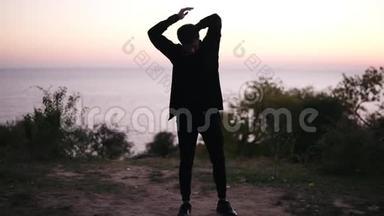 身穿黑色运动服的黑发青年男子正在热身，站在草地上伸展双臂。美丽的景色