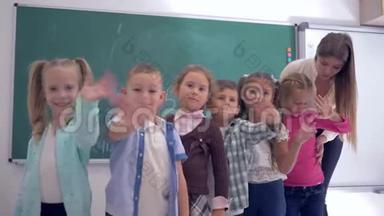 小学一组幼儿带着幼儿教师在教室的黑板背景上挥手