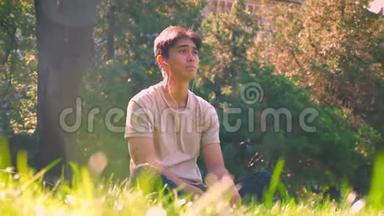 梦想中的亚洲男孩独自在公园里闲逛，坐在阳光下的草地上，清新的春天气氛