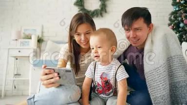 一个幸福的年轻母亲会自取其家。 有一个小儿子的年轻父母在智能手机上拍照
