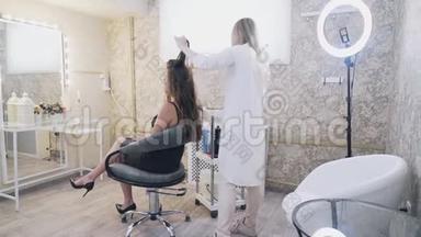 模特坐在化妆师的椅子上，造型师刷她的头发，旋转钳子上的卷发。 A.