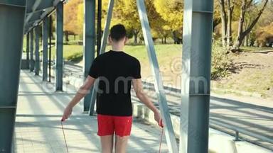 青年运动员在舒适的运动，适合跳跃的绳索上的运动场在平台附近的金属机架。 男孩