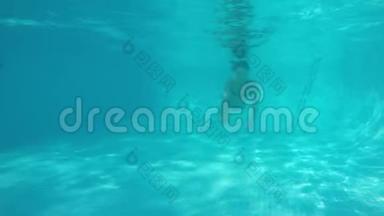 穿着蓝色比基尼的白人女孩在蓝色游泳池的镜头下游泳。 从水下观看