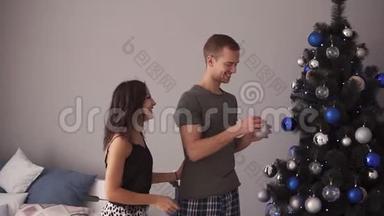 快乐的年轻夫妇<strong>装饰圣诞树</strong>。<strong>装饰圣诞树</strong>的年轻家庭。现代化的阁楼内部房间。爱