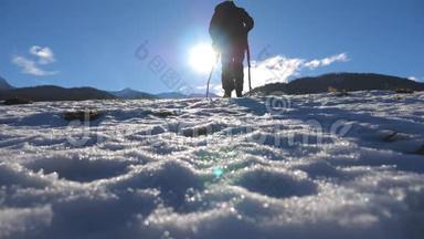 在阳光明媚的日子里，一个面目全非的家伙在雪地草地上用棍子走路。 年轻徒步旅行者在雪地上跋涉