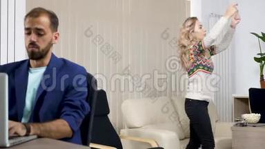 美丽的金发女人看电视，<strong>大声喧哗</strong>，而她穿着蓝色夹克的伴侣则试图在电脑上工作